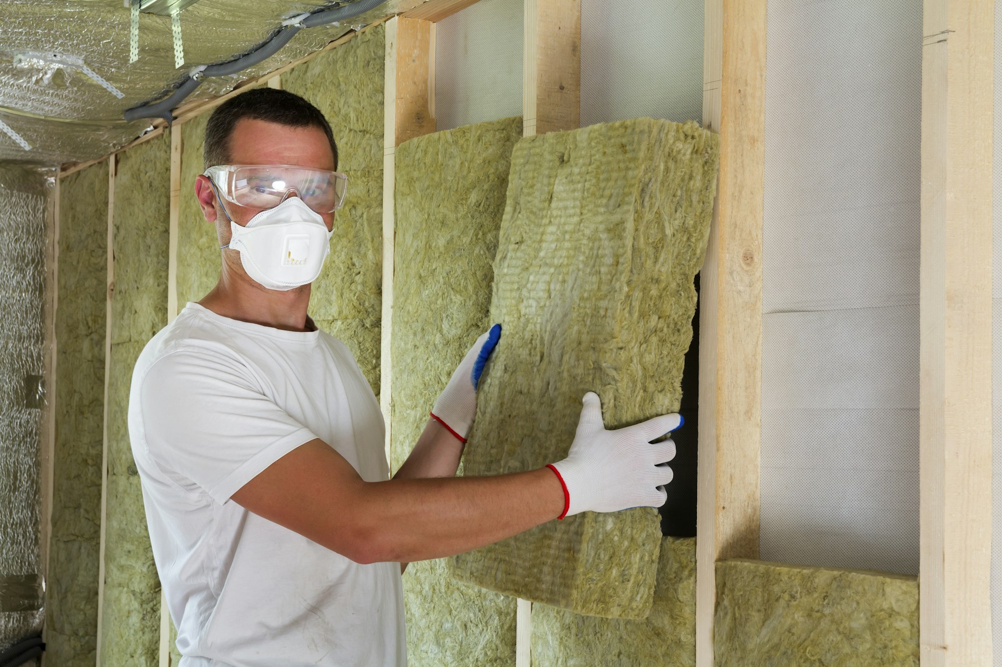 Worker in protective goggles and respirator insulating rock wool insulation